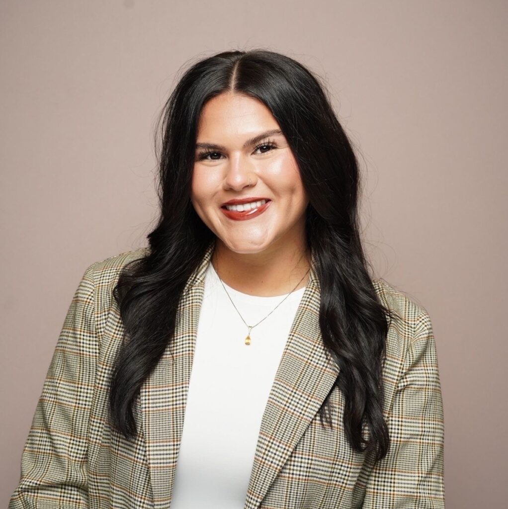 Confident woman with dark hair wearing plaid blazer and white top.