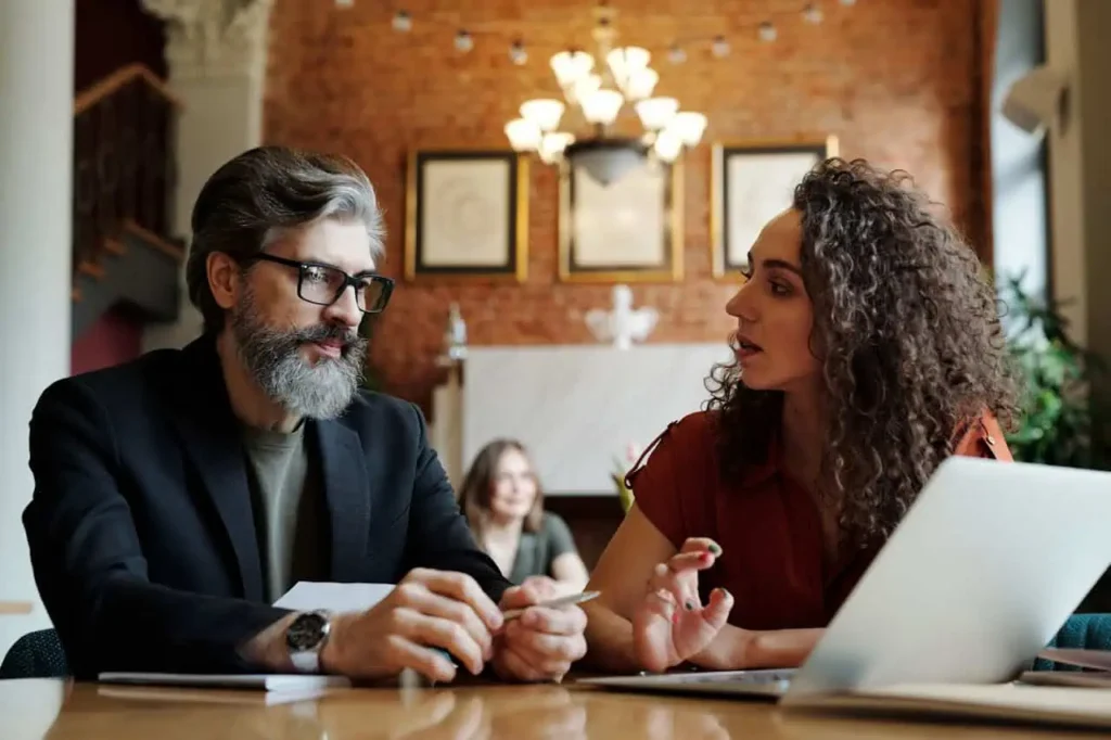 Man with beard discussing project details with woman in casual meeting.