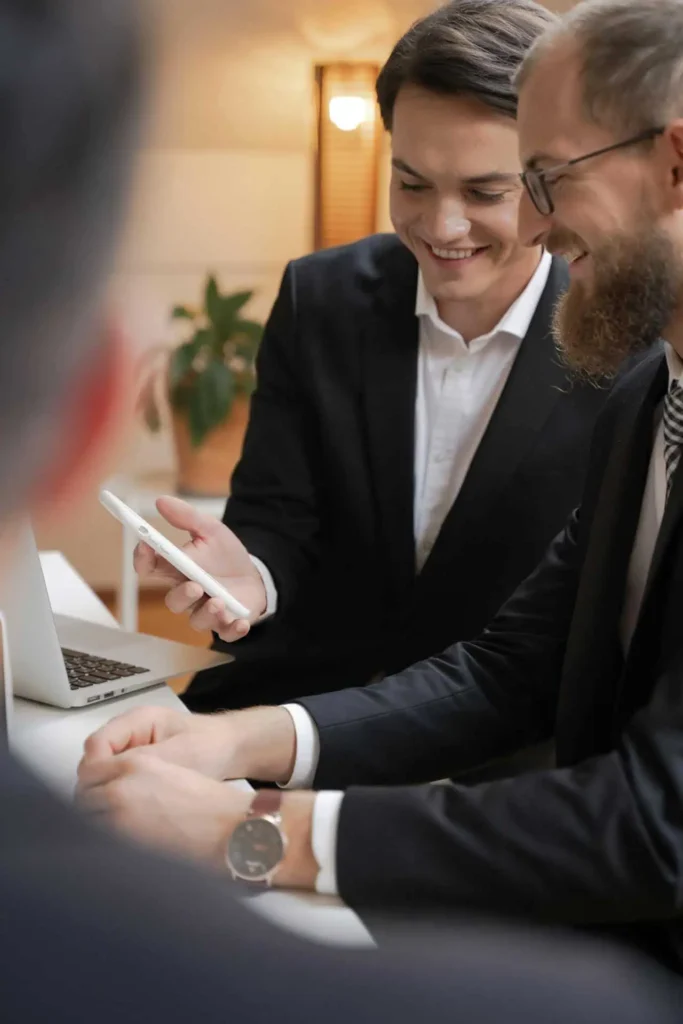 Colleagues in suits smiling while discussing something on smartphone together.